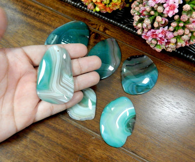 Green Drilled Freeform Agate Slices With Polished Edge in Hand on Wooden Background.