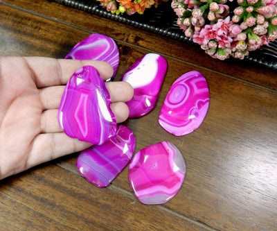 Pink Drilled Freeform Agate Slices With Polished Edge in Hand on Wooden Background.