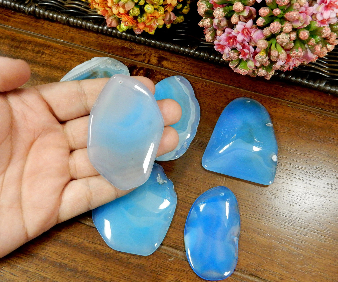 Light Blue Drilled Freeform Agate Slices With Polished Edge in Hand on Wooden Background.