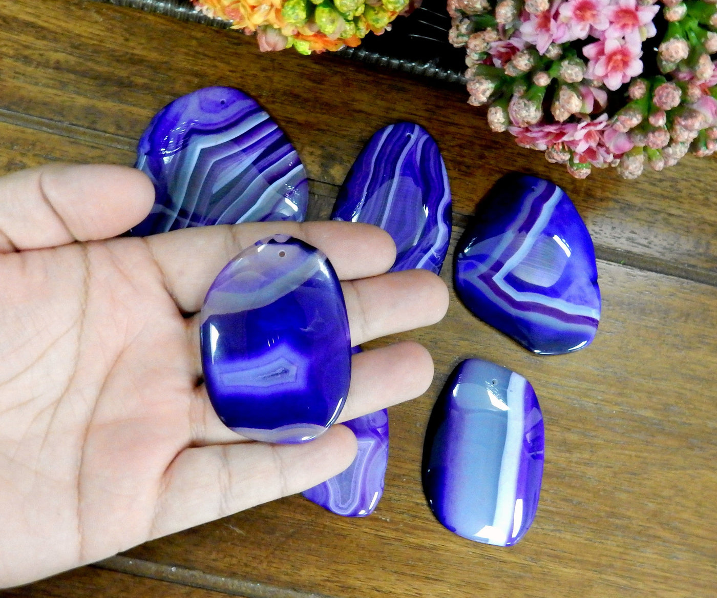 Purple Drilled Freeform Agate Slices With Polished Edge in Hand on Wooden Background.