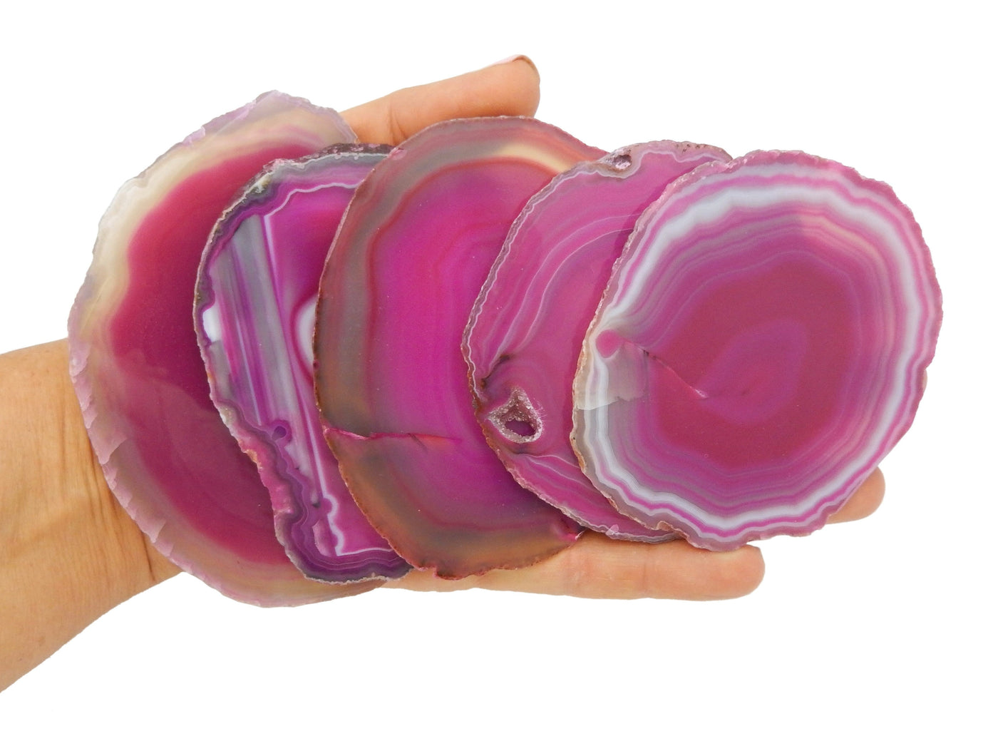 5 pink agate slices particial stacked and held in a hand.