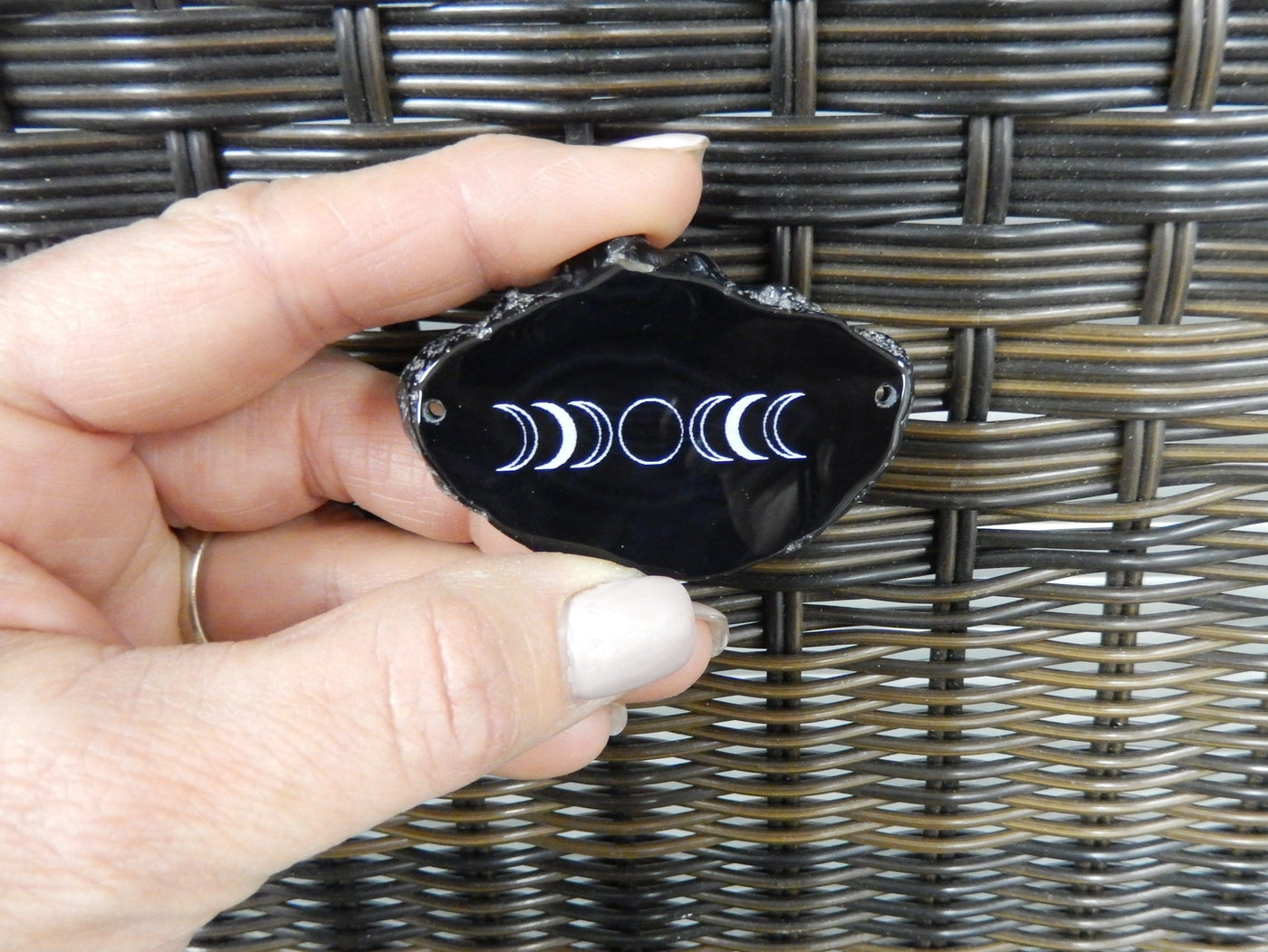 Picture of black double drilled agate slice, displayed in hand for hand reference.