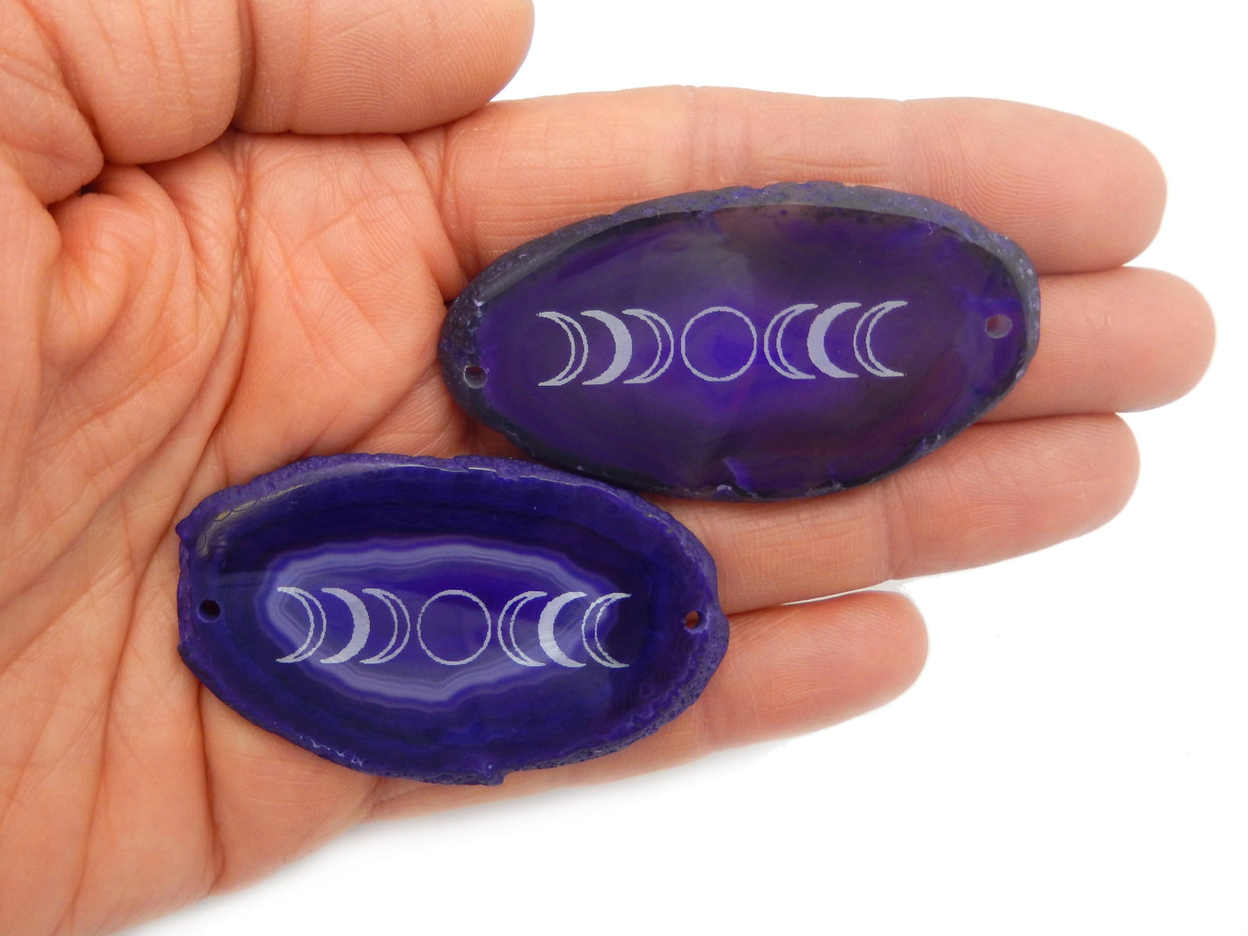 Picture of two of our purple agate slices double drilled being displayed in hand for size reference.