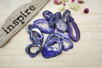 Multiple Dark Purple Geode Slice on Top Each other next to Inspire Wooden Piece Sign and Flowers on the Side on Wood background.