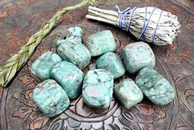 amazonite stones being displayed on a dark brown back ground, next to a sage bundle. 