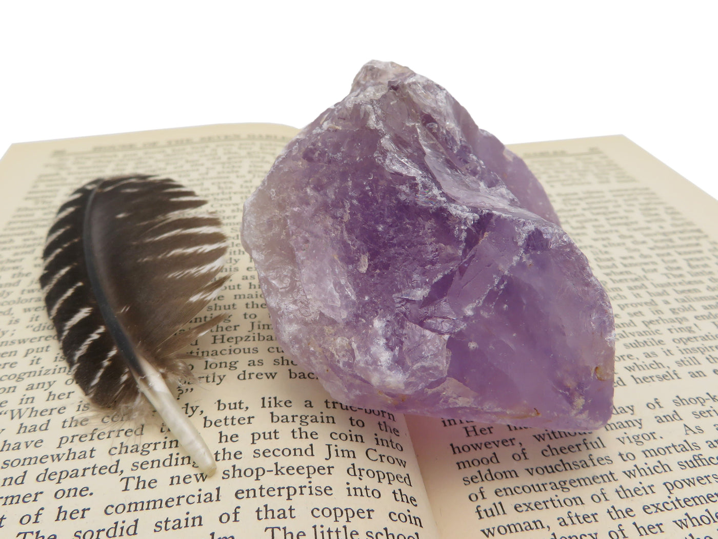 Natural Raw Amethyst Stone displayed on a book next to a feather. 