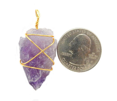 Picture of 1 arrowheads pedant wire wrapped gold tone on a white background, next to a quarter for size reference.