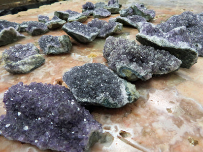 There are 3 Rows of amethyst clusters lined up next to each other in this picture. The amethyst Clusters are being displayed on a marbled surface. 