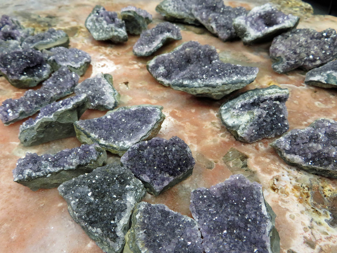 There are 3 Rows of amethyst clusters lined up next to each other in this picture. The amethyst Clusters are being displayed on a marbled surface.