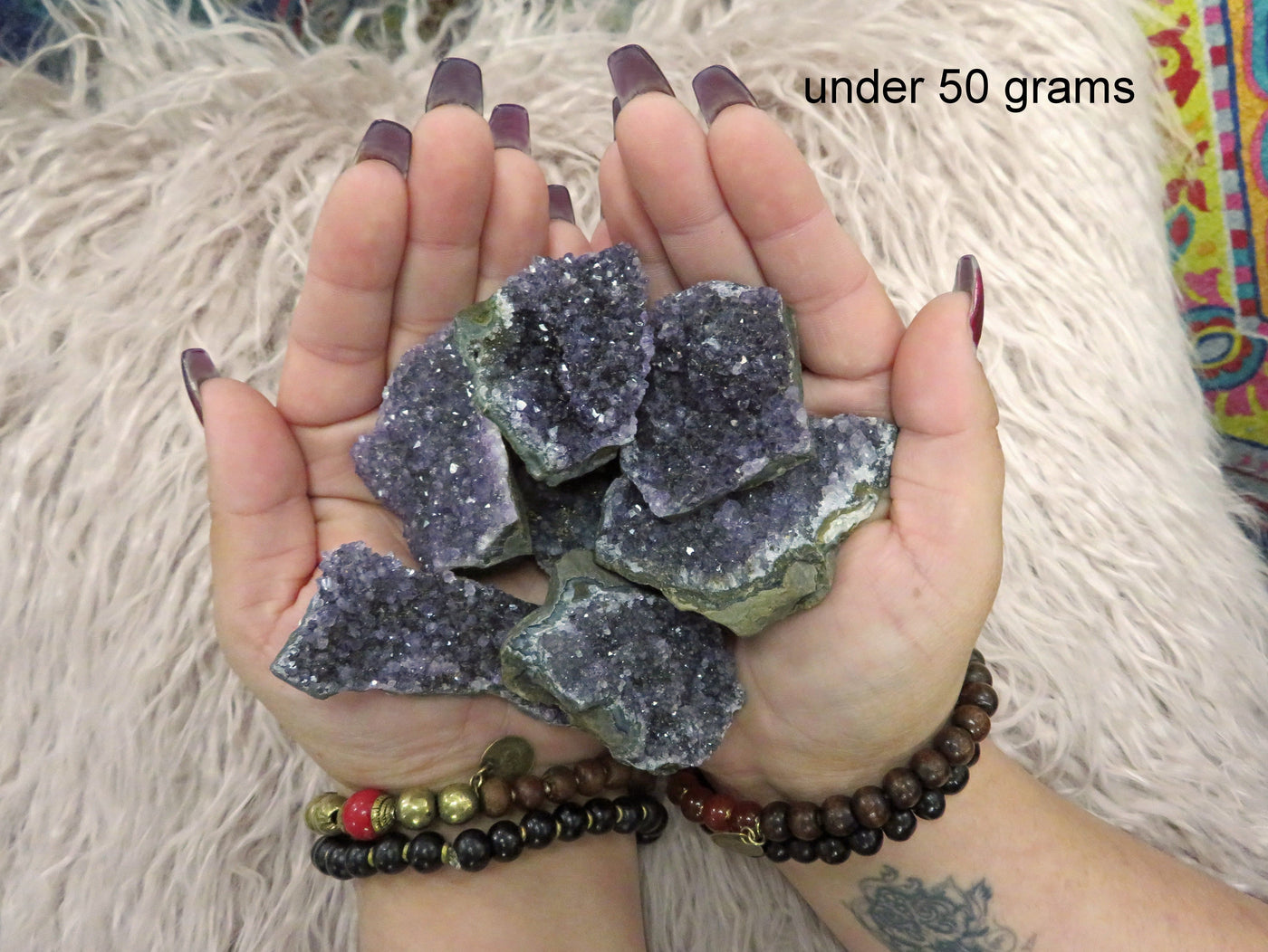 Multiple under 50 grams amethyst clusters are being held with both hands for size reference in this picture. 