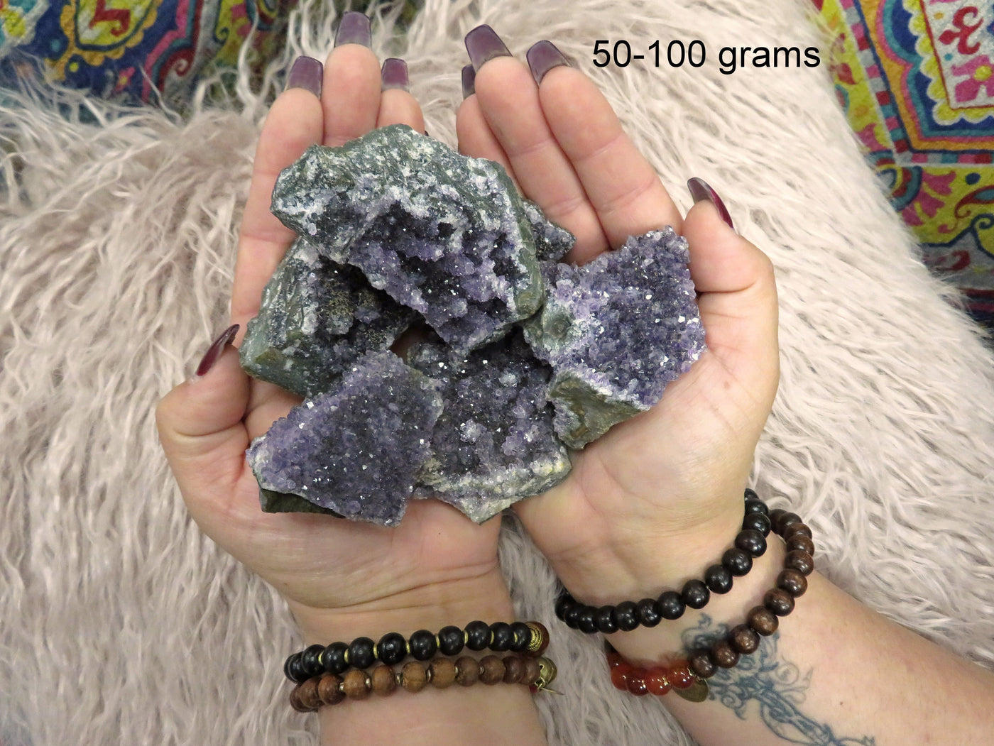 Multiple under 50 to 100 grams amethyst clusters are being held with both hands for size reference in this picture.