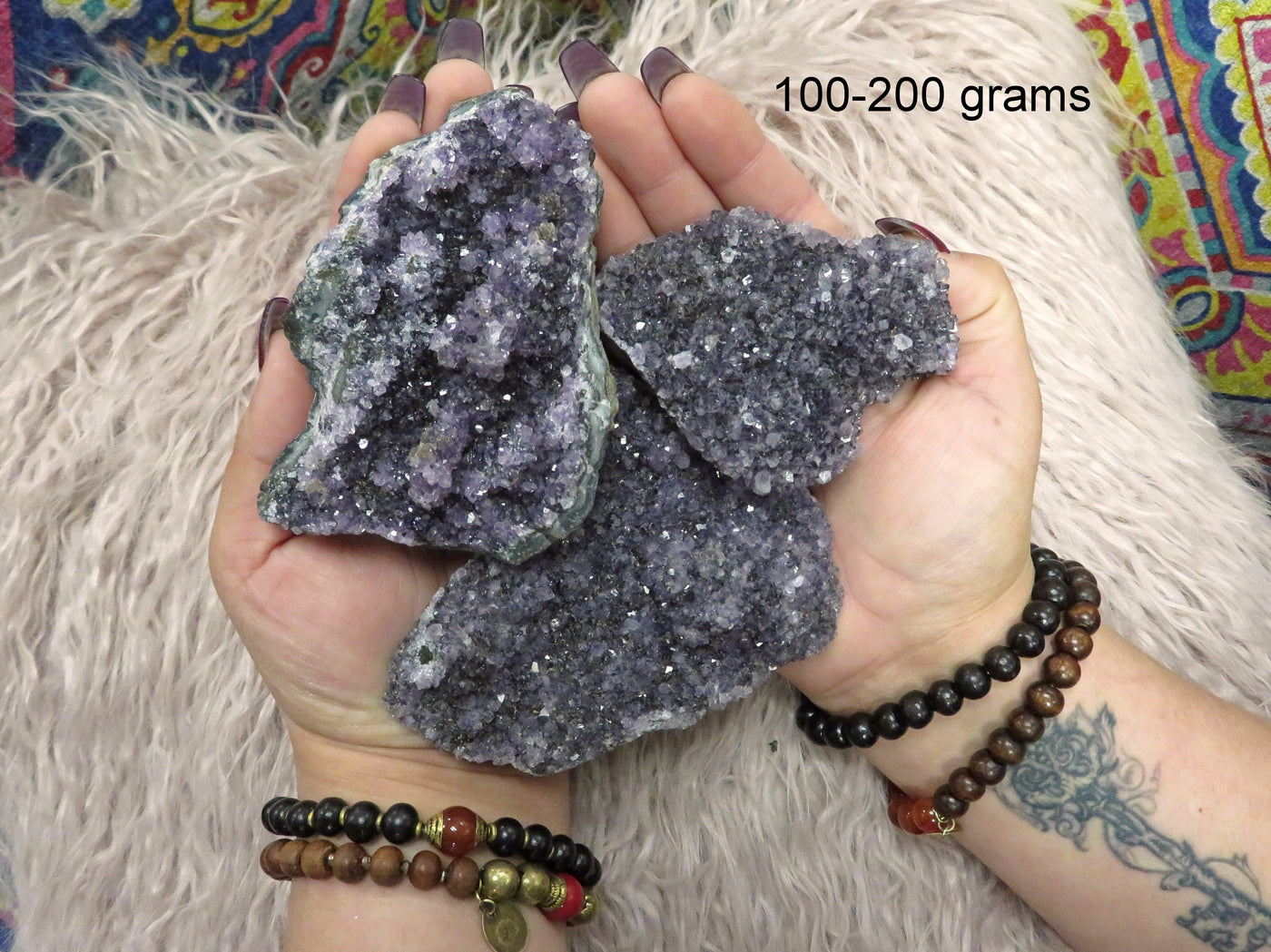 Multiple under 100 to 200 grams amethyst clusters are being held with both hands for size reference in this picture.