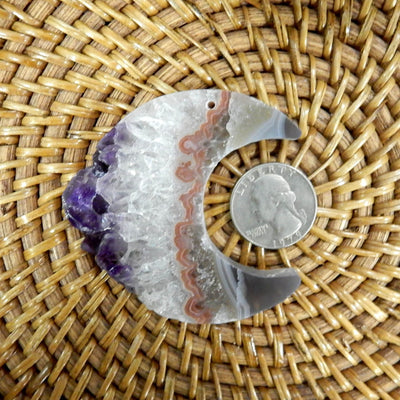 large drilled amethyst half moon with a quarter for size refrence and decorations in the background