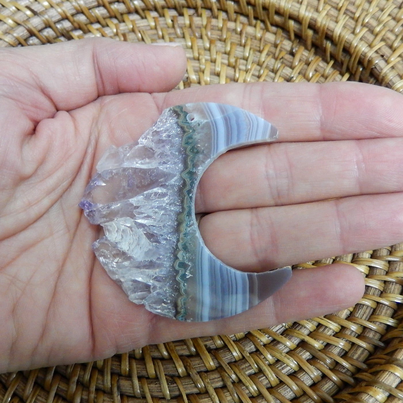 hand holding up large drilled amethyst half moon with decorations in the background