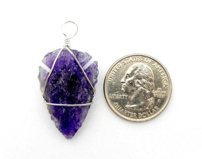 Picture of One arrowhead silver wire wrapped on a white background, next to a quarter for size reference.