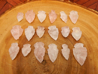 15 Rose Quartz Arrowheads lined up on slab of wood