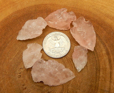 6 Rose Quartz Arrowheads surrounding a quarter for size comparison on wood slab