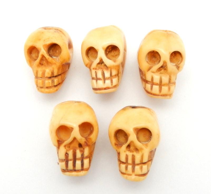 multiple top to bottom drilled skull shaped bone bead displayed on white background to show carving color texture differences