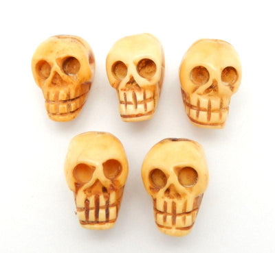 multiple top to bottom drilled skull shaped bone bead displayed on white background to show carving color texture differences