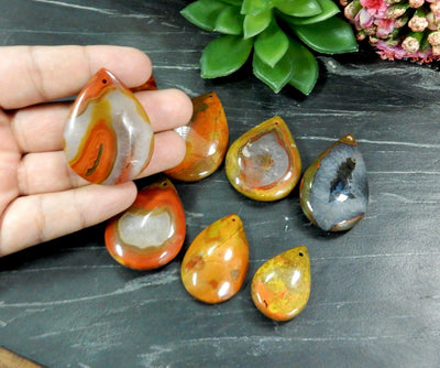 Hand holding up Red Chinese Agate Teardrop Shaped Bead with others on black background