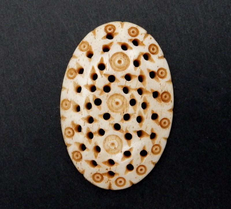 close up of one Carved bone oval cabochon on a black backgrond