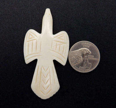 one carved bone cross next to a quarter on a black background