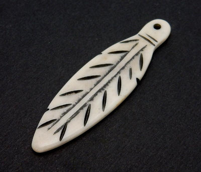 close up side view of a carved bone feather on a black background