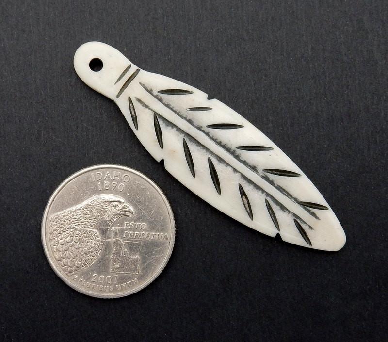 one carved bone feather next to a quarter on a  black background