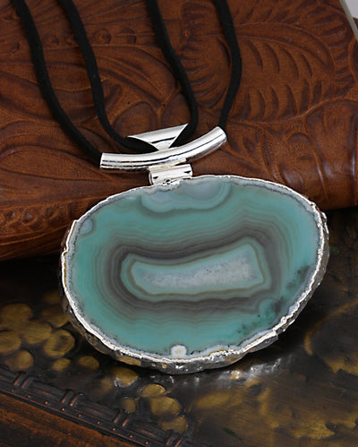 A green agate necklace with black leather cord and silver bail with a dark colored background.