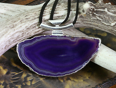 A purple agate necklace with black leather cord and silver bail with a dark colored background.
