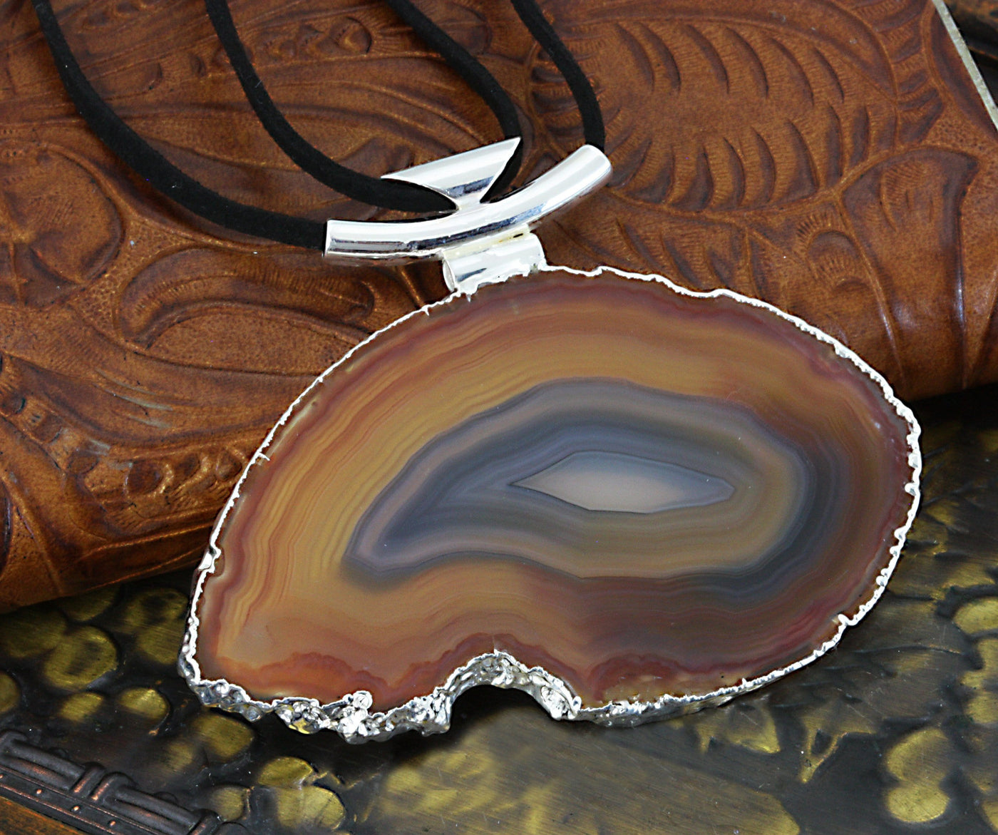 A natural agate necklace with black leather cord and silver bail with a dark colored background.