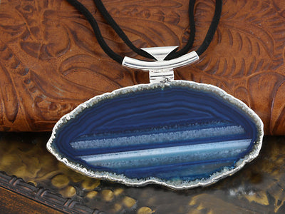 A blue agate necklace with black leather cord and silver bail with a dark colored background.
