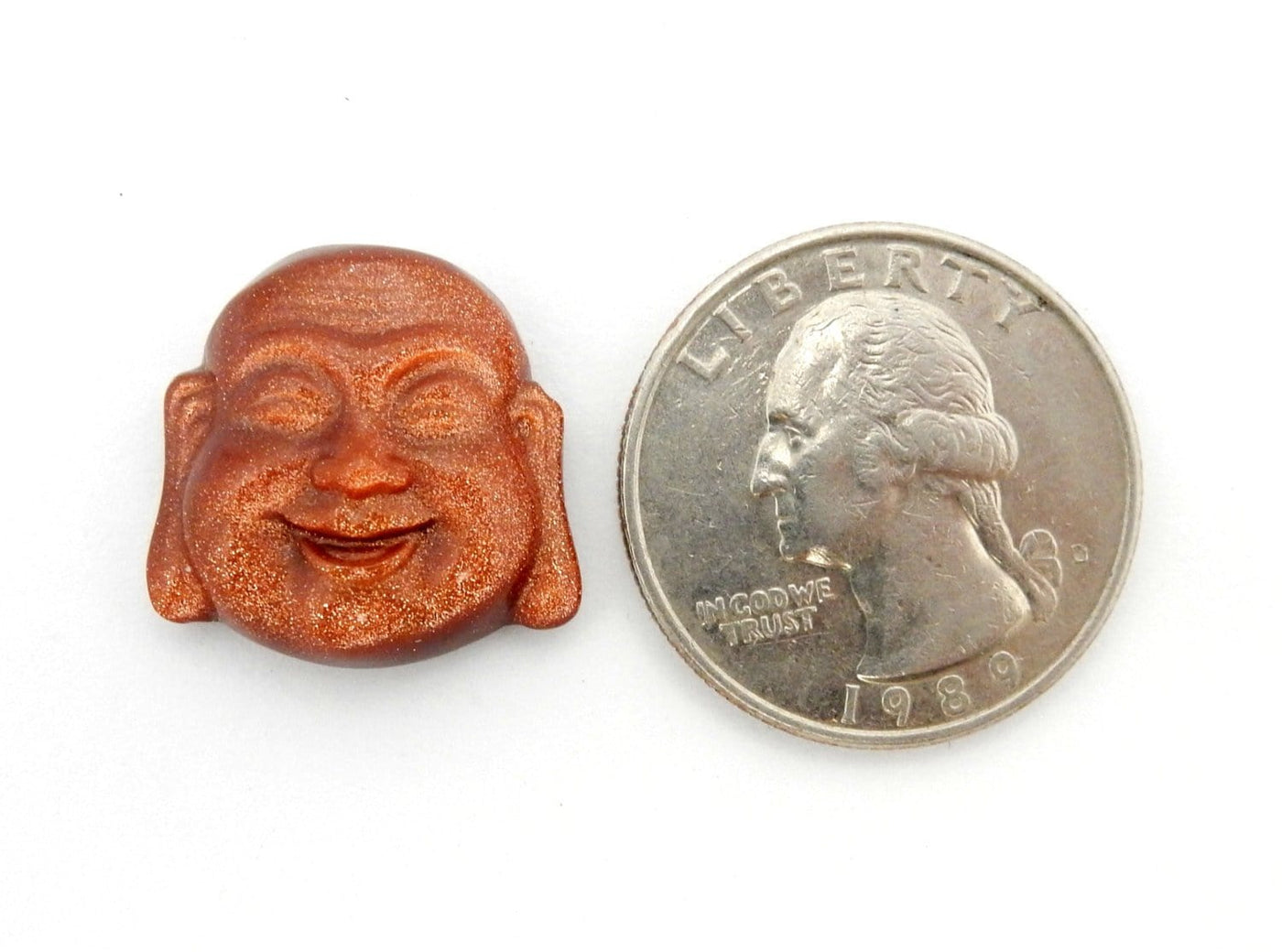 Goldstone Buddha Head Cabochon next to a quarter for size reference on white background