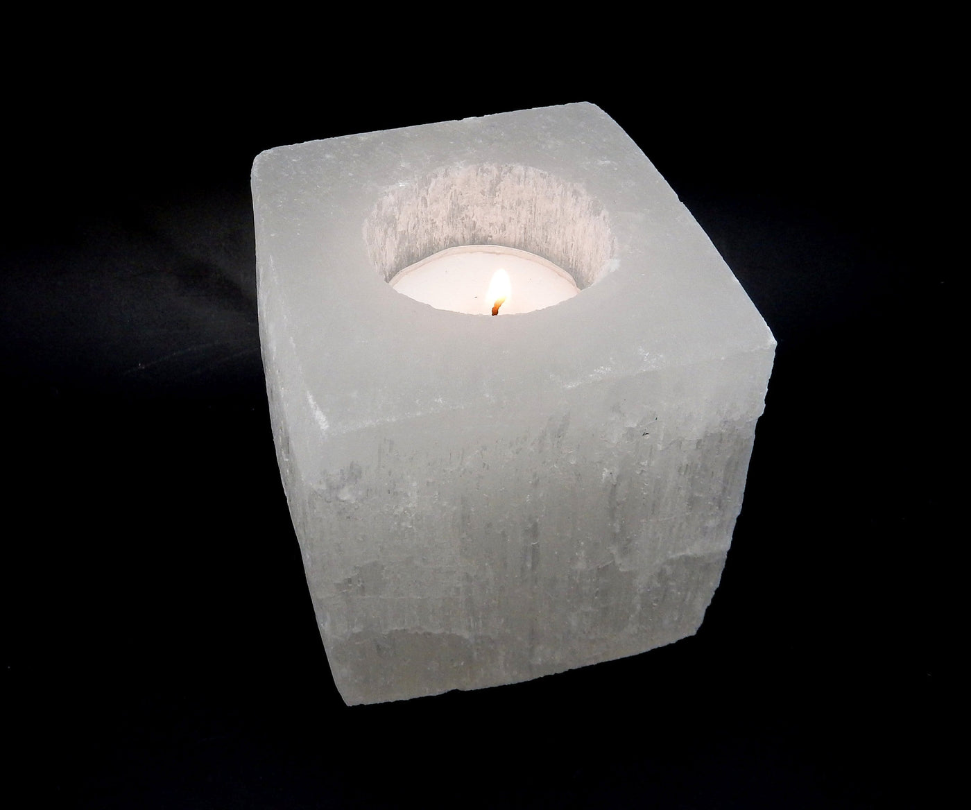 SIngle Square Shaped Selenite Candle Holder on a black background with a lit candle inside (candle not included)