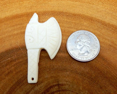 close up of carved bone axe head next to a quarter on a wood background