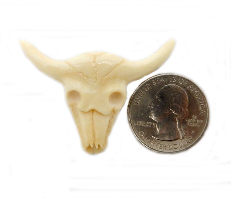 carved bone cattle head next to a quarter on a white background