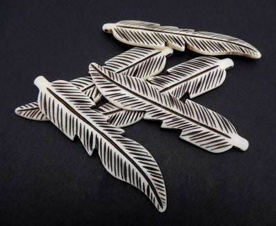 5 carved bone feathers stacked on top fo each other with a black background