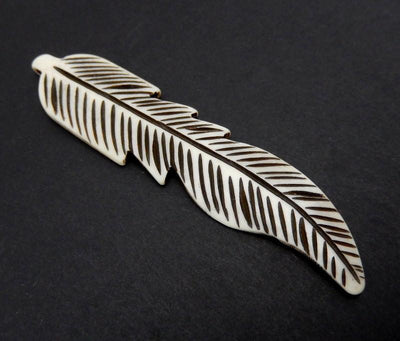 close up side view of a carved bone feather on a black background