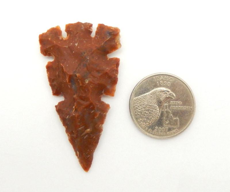 one jasper arrowhead next to a quarter on a white background