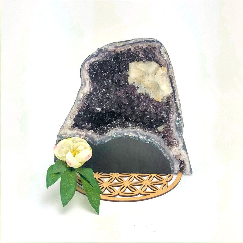 Amethyst geode on a white background on top of a crystal grid with a white flower next to it.