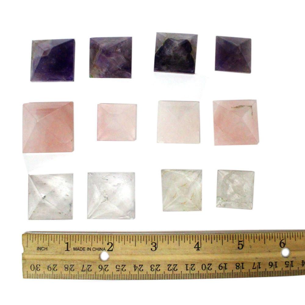 Assorted Crystal quartz, rose quartz, and amethyst pyramids on a white background with a ruler showing they are about 1 inch.