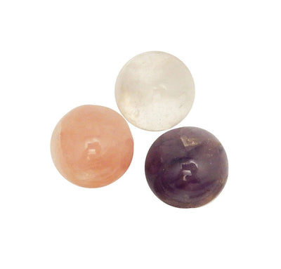 Photo of three spheres one in crystal quartz, one in amethyst, one in rose quartz on a white background.