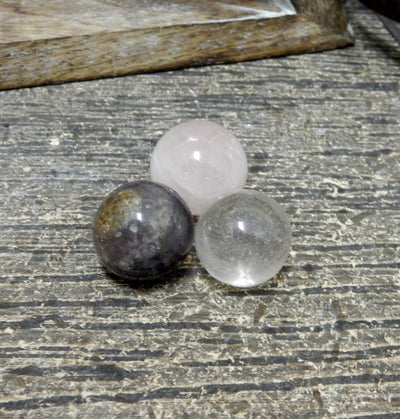 Photo of three spheres one in crystal quartz, one in amethyst, one in rose quartz on a brown wood background.