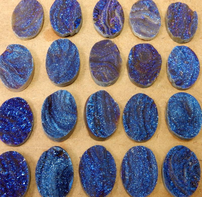 Mystic blue Titanium Chalcedony Druzy Oval Cabochons spread out on a table showing variation in druzy