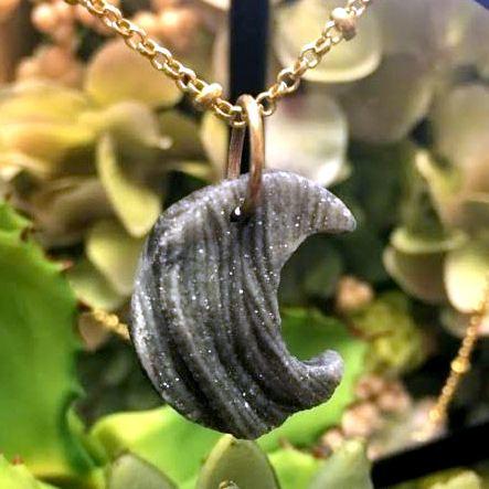 Raw Chalcedony Moon Crescent on necklace chain with plants blurred in the background