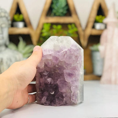 hand next to Amethyst Druzy Polished Tower Point with decorations blurred in the background