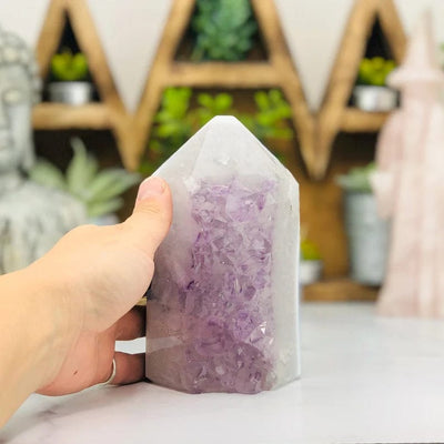 hand next to Amethyst Druzy Polished Tower Point with decorations in the background