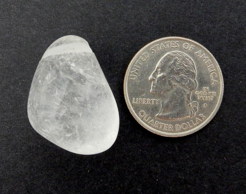 Drilled Tumbled Stone Crystal Quartz Polished Bead Next to a Quarter on Black Background.