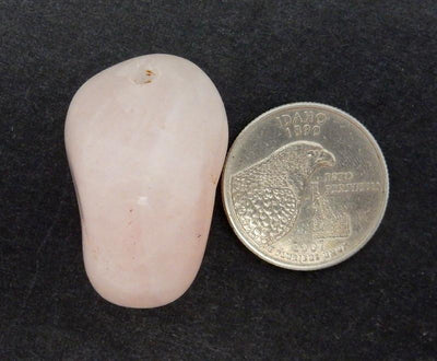 Drilled Tumbled Stone - Rose Quartz Beads--Close up view of drilled Tumbled Stone Rose Quartz Beads next to a Quarter compared for size reference on Black Background.
