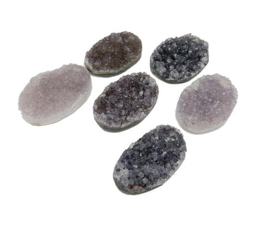 Assorted druzy in shades of white, gray, purple, and black on a white background.  They are drilled on both edges.